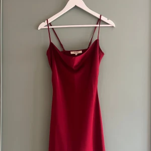 Röd satinklänning - Röd satinklänning med spagettiband. I storlek XS men är ganska lång så beroende på hur kort man vill ha den passar den även Small.  Oanvänd, som ny! Originalpris 750kr.