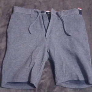 Grå shorts från SMOG - Säljer ett par snygga grå shorts från SMOG i storlek XS. De har en stilren design med dragsko i midjan och praktiska fickor både fram och bak. Perfekta för sommardagar eller en avslappnad vårlook. Materialet känns bekvämt och är lätt att matcha med olika outfits.