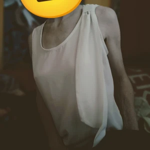 Vit topp från Mireille - Säljer en elegant vit topp från Mireille. Den har en unik design med en knutdetalj vid axeln och är ärmlös. Perfekt för både vardag och festliga tillfällen. Materialet känns mjukt och luftigt.