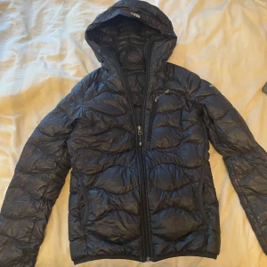 Svart dunjacka från The North Face - Säljer en svart dunjacka från peak performance . Den är supervarm och perfekt för kalla vinterdagar. Jackan har en dragkedja framtill och en mysig huva. Den är i bra skick och redo för nya äventyr!