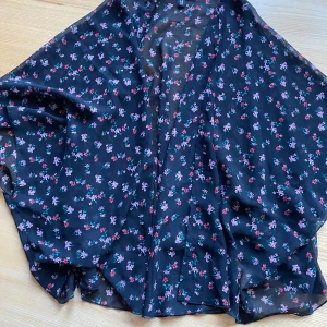 Blommig kimono från H&M Divided - Säljer en superfin och luftig kimono från H&M Divided. Den är svart med ett blommigt mönster i rosa och lila nyanser. Perfekt att ha över en topp för en extra touch. Passar bra till både vår och sommar!