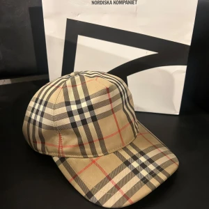 Burberry Keps - En mycket fin Burberry keps i storlek M. Kepsen är i bra skicka, dock använd men inga skador förekommer. Tveka inte på att buda!!