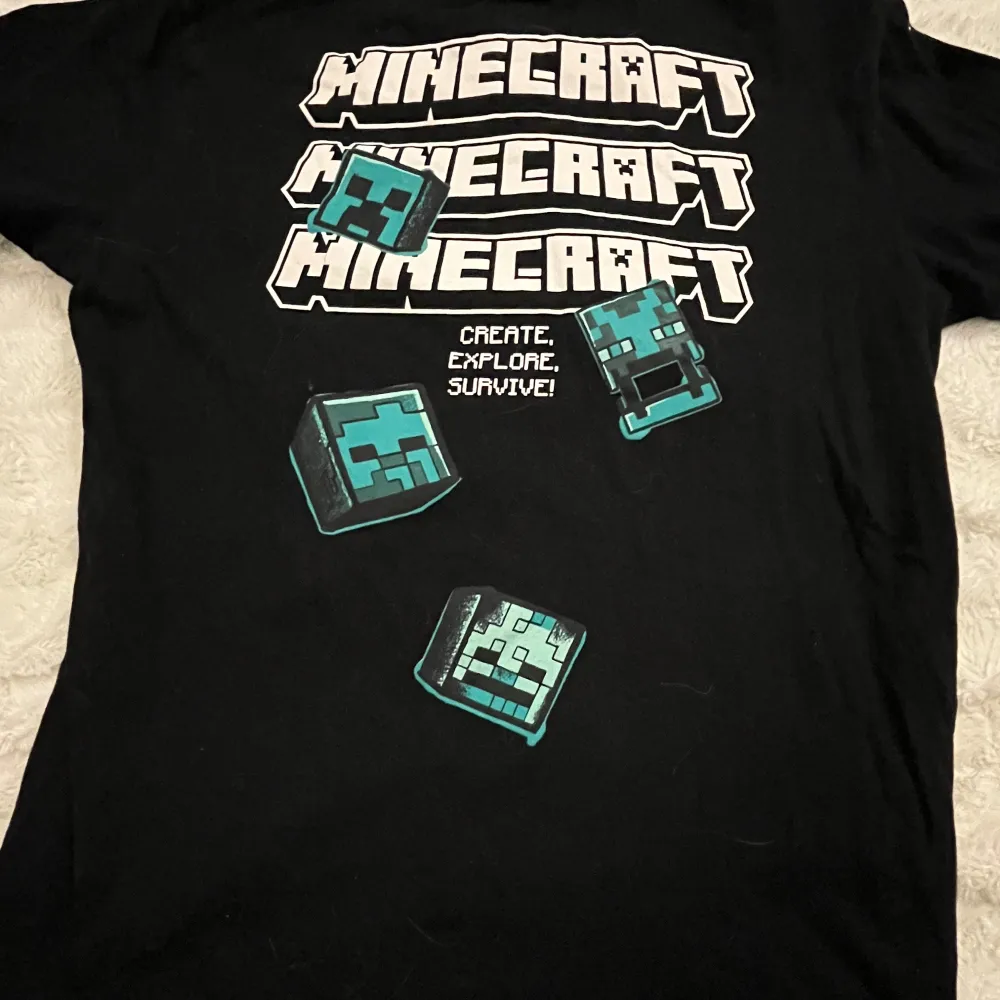 Säljer en svart t-shirt med coolt Minecraft-tryck från Kappahl i storlek 158/164. Den har korta ärmar och är perfekt för alla fans av spelet. Trycket visar olika karaktärer som Creeper och Zombie i blått och grönt. Perfekt för vardagsbruk eller gamingkvällar! 🎮. T-shirts.