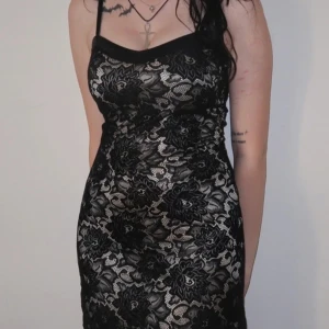 Svart spetsklänning med blommönster - Säljer en elegant svart spetsklänning med blommönster. Klänningen är tight och har smala axelband. Perfekt för festliga tillfällen. Den har en vacker spetsdesign som ger en sofistikerad look.