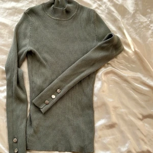 Grön ribbad polotröja - Säljer en snygg grön ribbad polotröja i storlek XS. Tröjan har långa ärmar och stilrena knappar vid ärmsluten. Perfekt för höst och vinter, både mysig och trendig! 🍂