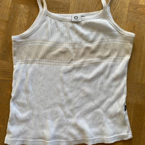 Vit ribbad linnetopp från Connect - Säljer en vit ribbad linnetopp från Connect i storlek 42/44. Toppen är i 100% bomull och har smala axelband. Perfekt för sommardagar eller som ett basplagg i garderoben. Använd men i bra skick!