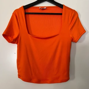 Orange topp från Amisu - Säljer en snygg orange topp från Amisu i storlek L. Den har en fyrkantig urringning och korta ärmar, perfekt för sommardagar. Toppen är i ett stretchigt material som sitter bekvämt. Perfekt för en casual look eller att styla upp för en utekväll! 🧡There is little pen dot on the bottom of the shirt, as you can see on the last picture ❤️
