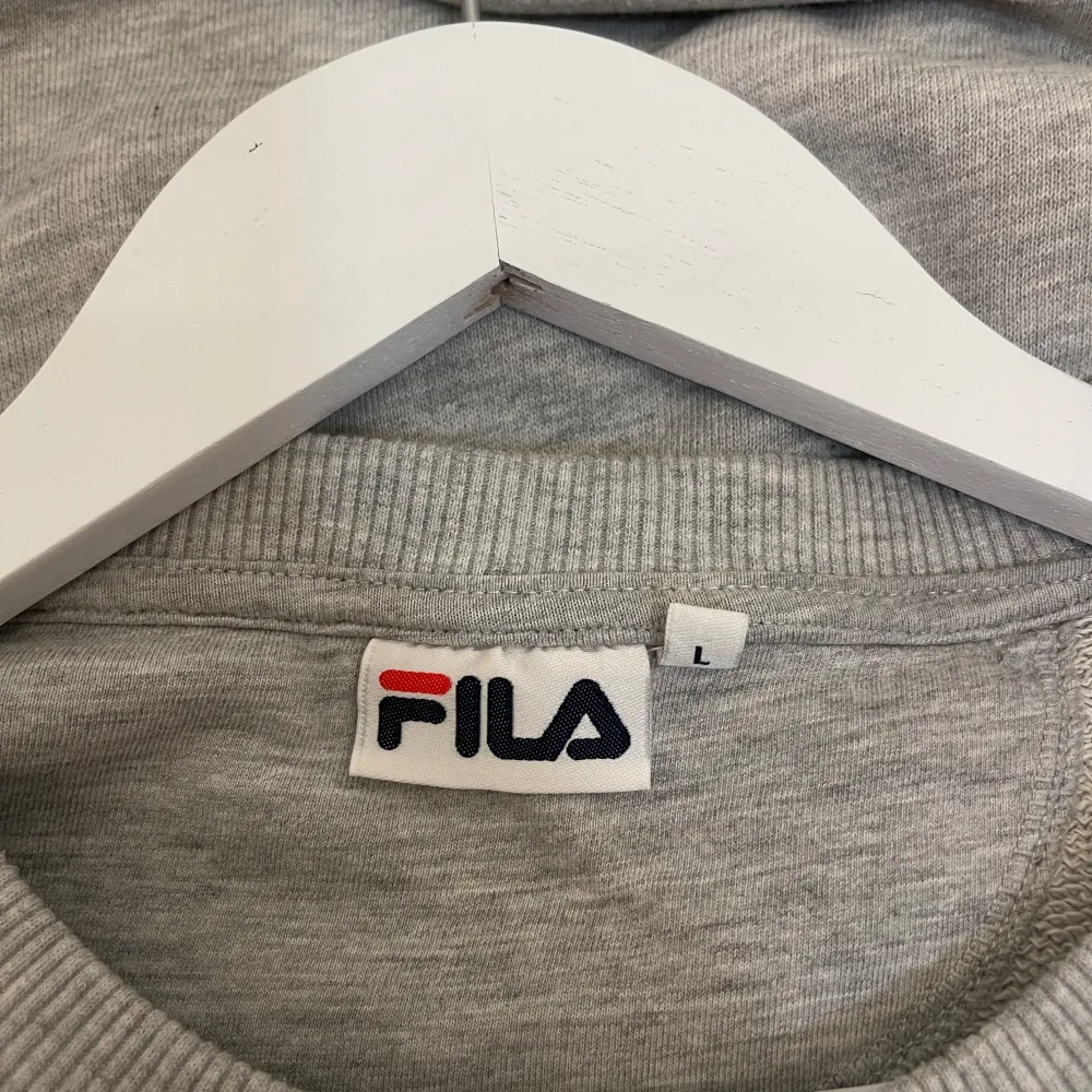 Säljer en stilren grå sweatshirt från Fila i storlek L. Tröjan har en klassisk rund hals och ett stort Fila-logotyp på bröstet. Perfekt för en avslappnad stil eller träning. Den är i bra skick och superbekväm att ha på sig. Passar både till vardags och sportiga aktiviteter.. Tröjor & Koftor.