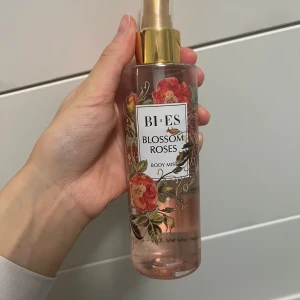 Blossom Roses Body Mist från Bi-Es - Säljer en body mist från Bi-Es med doften Blossom Roses. Flaskan är genomskinlig med ett vackert blommönster i rött och grönt. Den har en guldig spraytopp som ger en lyxig känsla. Perfekt för att fräscha upp sig under dagen! 🌹✨
