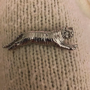 Silverfärgad tigerbrosch - Säljer en cool brosch i form av en tiger i silverfärg. Perfekt för att ge din outfit en unik touch! 🐯 Den är i nyskick och passar både till vardags och fest. Fäst den på din jacka eller väska för en extra stilpoäng.