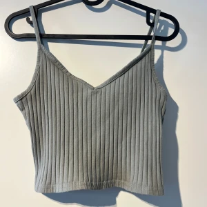 Grå ribbad linnetopp från H&M Divided - Säljer en snygg grå ribbad linnetopp från H&M Divided i storlek S. Toppen har smala axelband och en v-ringad design, perfekt för sommardagar eller som ett lager under en jacka. Den är i bra skick och superbekväm att bära. Passar till både vardag och fest!