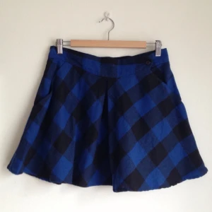 Blå/svart-rutig kort kjol med vidd och hög midja. 25% ull.  - Blå/svart-rutig kort kjol med vidd och hög midja. 25% ull. 