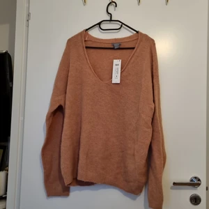 Lindex stickad tröja  - Stickad tröja, mixar material varav 30% ull och 21% alpacka.  Oanvänd, med prislapp kvar. Inköpt på Lindex. Färgen nånstans mellan rosa till svag orange. 