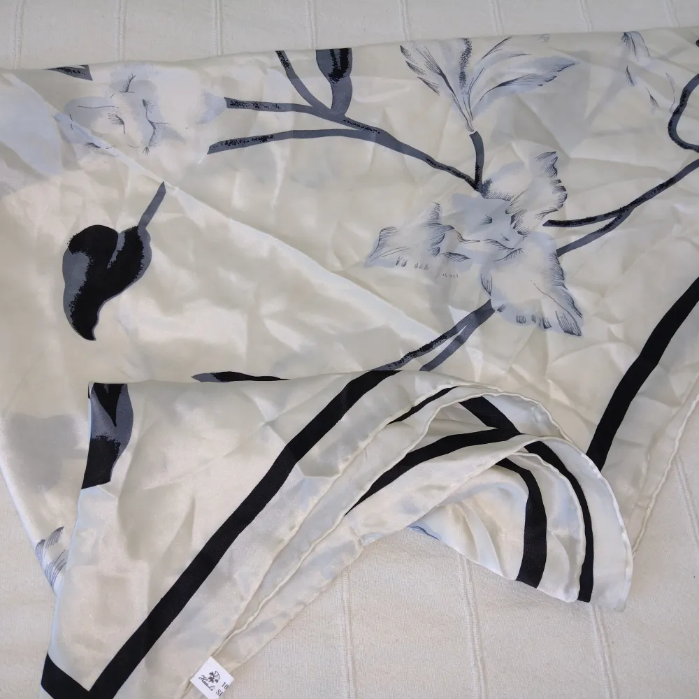 Hua Li 100% silk sjal i fint skick. Underbart mönster. Pärlemorfärgad botten och mönster i svart/grått/ljusblått. Den är stor (ca 108x108 cm) och skulle kunna användas som långkjol, knyttopp m.m. Handsydda fållade kanter. . Accessoarer.
