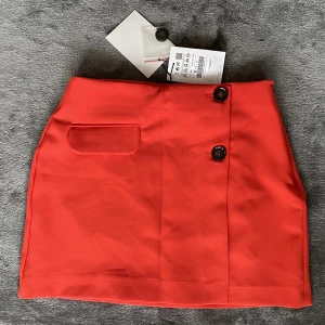 Ny rödorange minikjol - Jättefin röd minikjol med hög midja. Den har lite orange glans också beroende på ljuset. Aldrig använd med lappar kvar. Den har en stark färg så att den är perfekt till sommar! Säljer då jag rensar min garderob. Storlek 34/xs. 