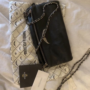 Zadig & Voltaire väska - Slitage i metallen där den silvriga färgen släppt. Annars i bra skick.  Komplett väska med båda banden samt dustbag. 