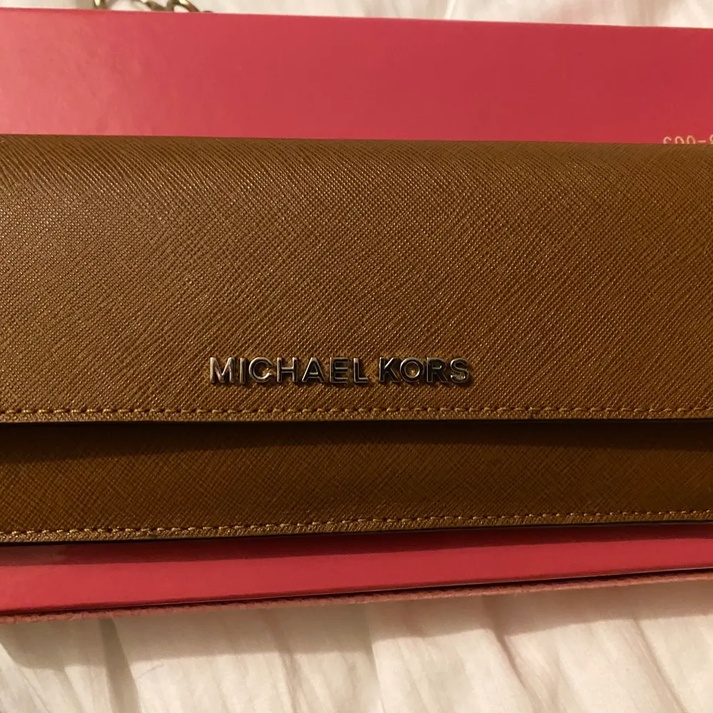 En helt ny, oanvänd Michael Kors plånbok som köptes hastigt i USA.  Perfekt skick då denna är oanvänd.  Röd intill och en fin brun förg utpå.. Väskor.