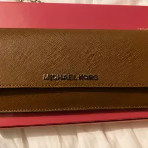 En helt ny, oanvänd Michael Kors plånbok som köptes hastigt i USA.  Perfekt skick då denna är oanvänd.  Röd intill och en fin brun förg utpå.