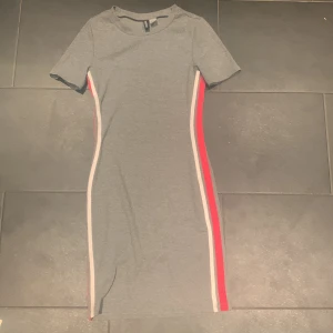 Grå klänning med ränder på sidan  - Grå tight klänning med en röd och en vit rand på båda sidorna 