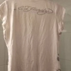 Ed Hardy  - Säljer en T-shirt med märket Ed Hardy. Denna är vit med mönster i svart och silver. Skön och töjbar, fin passform.