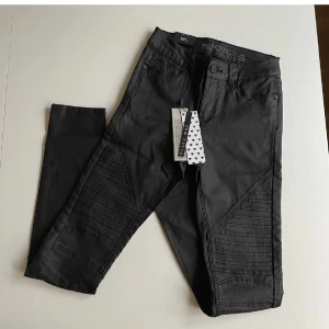Vaxade byxor strl XS/30 - Ett par vaxade byxor från Noisy May i storlek XS/30. Smal modell i stretchdenim med blank yta. Infällning fram på låret med sydda, små veck och smala ben samt smala benslut. Aldrig använda, lapparna är kvar(nypris 380:-). Midja:68cm Innerben:74cm