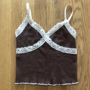 Brunt linne med spets  - Ett brunt linne med beige spets från Urban Outfitters! Skriv om du har frågor eller vill ha fler bilder. Köparen står för frakt. Kan mötas i Stockholm