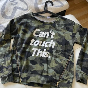 Camo tröjja S dragkedja text  - Skön tunnare tröjja i grön/grå camo med text :Can’t touch this” Stl S. Bomull tvätt 40 grader. Snygga detaljer med dragkedjor nedtill