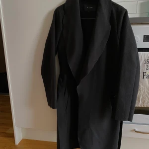 Vila kappa  - Klassisk, tidlös kappa från VILA med knytband.  - Två framfickor - Knytbandsstängning - Längd från axel bak: 93 cm i storlek 36