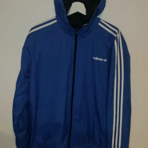 Adidas tunn två-i-ett jacka. St L - Adidas jacka som kan användas på två olika vis, antingen så den är helblå eller svart/blå,vit. Hittar ingen storlek men använts av en som använder L i kläder.   Obs! Finns en liten fläck som syns när jackan är i svart/blå,vit sidan. Obs! ... utöver det är skicket helt och fint. 