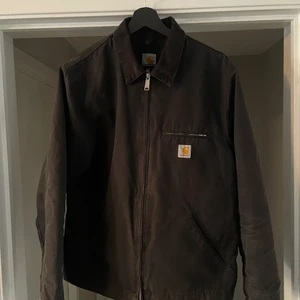 Carhartt Detroit Jacka - Säljer en klassisk svart Detroit-jacka från Carhartt. Den svarta färgen har börjat bli solblekt vilket gör att den får den där schyssta looken. Den är lätt bomullsfodrad i svart.  Jackan är märkt XL men jag upplever den mer som en L.  Måtten är, Pit to pit: 59 cm (23,2 inch) Längd från undersidan av kragen: 70 cm (27,5 inch)  Inga hål eller revor i tyget. Det enda är att innerfodret har släppt lite vid innerfickan.  Skickas mot fraktkostnad eller hämtas i Nyköping.