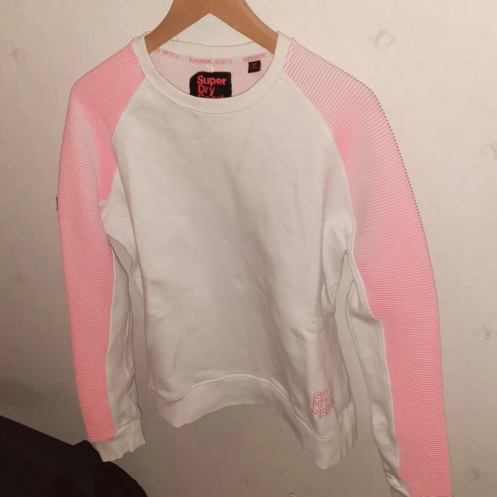 Vit Superdry Sport tröja med rosarandiga ribbade ärmar. Fint skick. Storlek M / EU 40. Kan hämtas i Stockholm, annars står köparen för frakt :). Skjortor.