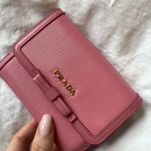 Prada - Äkta rosa Prada plånbok. Väldigt rymlig. Aldrig använd av mig. Den är som helt ny. Köpt på auktion. Skriv för fler bilder och jag kan visa vart den är köpt som äkthetsintyp. Fraktkostnad ingår. Kan även mötas upp i Sthlm 