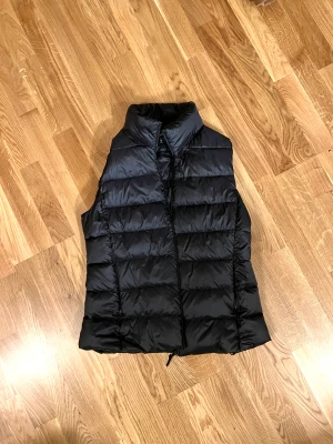 Uniqlo Puffer Vest i svart - Säljer denna supersnygga, minimalistiska puffer väst från Uniqlo.  Perfekt för träning och promenader!