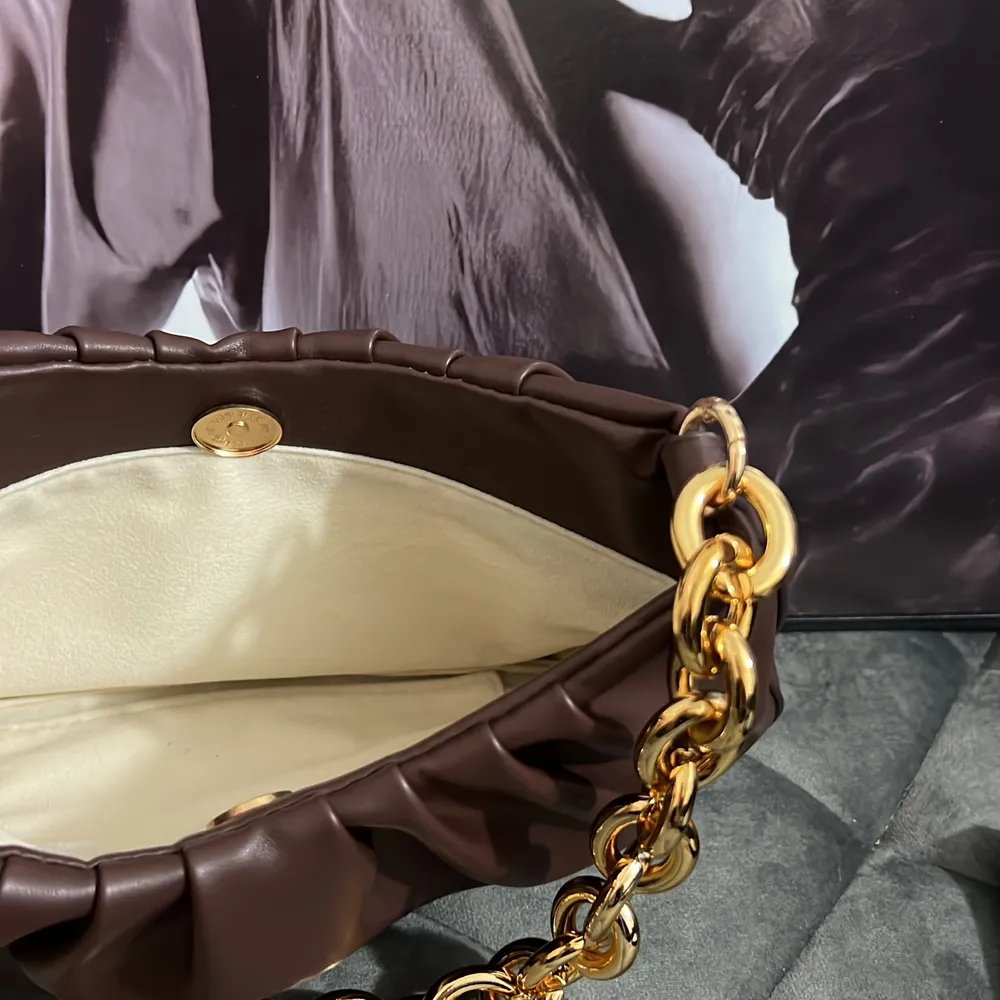 En brun axelväska med guld detaljer . Väskor.