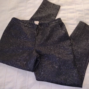 Skimriga svarta kostymbyxor, ankelmodell, storlek 36 - Väldigt coola och festliga kostymbyxor i ankelmodell. Tyget har ett snyggt mönster och struktur och är skimrigt/shiny ✨ Två fickor i fram och en i bak. Perfekta till jul- och nyårsfester. 