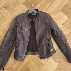 Brun läderjacka - Jofama By Kenza - Snygg brun läderjacka i vintage modell.  Säljes pga har blivit för tight för mig. En tight modell! Två fickor med dragkedja på sidorna, en med knapp på bröstet och två innerfickor.  400 inklusive frakt!