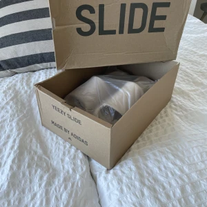 Yeezy Slide Pure strlk 42  - Hej! Säljer nu mina jättefina Yeezy Slides då jag har växt ur dem, Jag har använt dem fåtal ggr och dem är i jättefint skick.  Perfekta tofflor att ha på sommarn när man ska bada och vara på stranden. Äkta vara. Vill bli av med dem så fort de går 900kr 