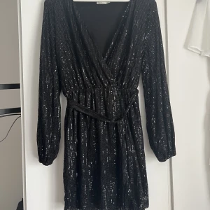 Klänning - En svart glittrig klänning i stl M med ett tillhörande skärp som går att ta bort. Använd en gång och några paljetter har lossnat men inget som man tänker på. Nypris 599