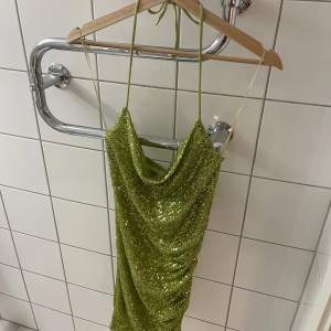 Helt oanvänd klänning från bikbok i glittrande grön och knytning i nacken, storlek XS. Lapparna på! Köpt för 399kr