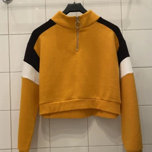 Gul Svart Vit tjocktröja med dragkedja  - Gul, vit och svart tröja från H&M med större krage och dragkedja. Storlek M. Från rökfritt och djurfritt hem. Kan mötas i Centrala Stockholm eller frakta. Skriv vid frågor eller intresse! 