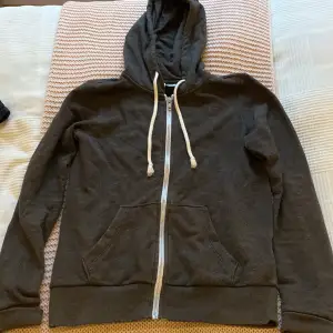 En fin grå hoodie med blixtlås från HM. Den har en grå luva med vita snören. Den har även en ficka ungefär på magen som går ihop. Storlek XS. Pris kan diskuteras!