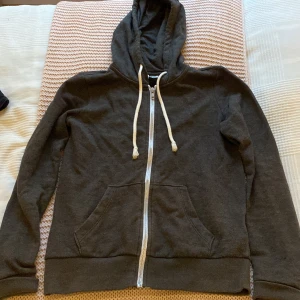 Hoodie med blixtlås  - En fin grå hoodie med blixtlås från HM. Den har en grå luva med vita snören. Den har även en ficka ungefär på magen som går ihop. Storlek XS. Pris kan diskuteras!