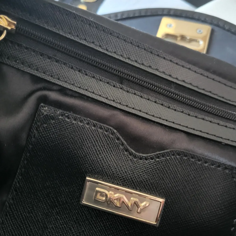 Nypris: 1699 kr. Mått: Ca 30 cm bred. DKNY väska med gulddetaljer, handtag och justerbar axelrem/crossbodyrem i läder. Dustbag medföljer. Rymmer mycket! Nåt pyttelitet märke på baksidan. Annars 100% nyskick, även DKNY-hänget.. Väskor.