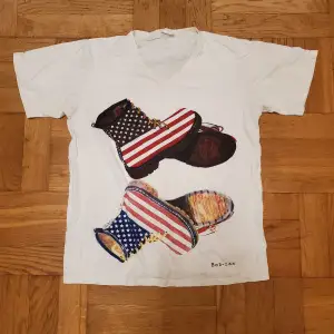 T-shirt med tryck av Dr Martens-liknande kängor med amerikanska flaggan på. Sparsamt använd, fint skick. Okej att komma med bud. Katt i hemmet. 