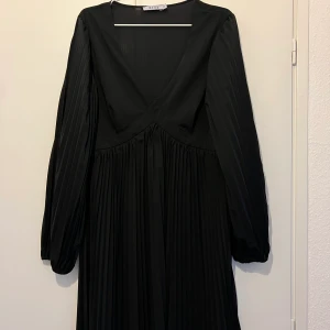Svart plisserad klänning från NA-KD - Svart plisserad klänning med v-ringning från NA-KD med dragkedja på sidan. Använd fåtal gånger så i gott skick. För mer information och bilder kontakta mig.