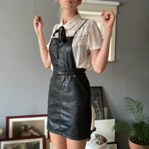 Skinnklänning - Klänning i fuskskinn med justerbara band och fickor.  Frakt tillkommer.