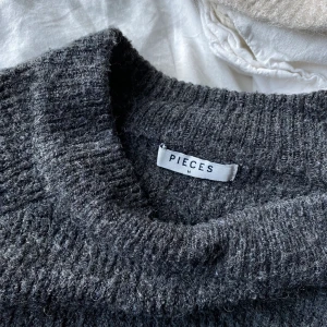 Grå stickad tröja - En mörkgrå stickad tröja från Pieces. Använt skick. Lite tunnare tröja men fortfarande varm. I storlek M men skulle säga att den är mer som en S