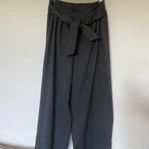 Byxor från Zara - Säljer ett par hödmidjade kostymbyxa-liknande byxor med knytdetalj från Zara. Mörkgråa.  De är i storlek small och i super fint skick. Ingen stretch men dragkedja i sidan av midjan. 