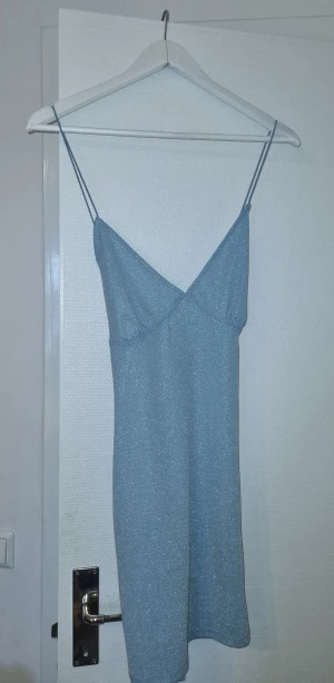 Glittrig miniklänning - Helt ny minidress, perfekt till fest då den är väldigt glittrig. Endast testad. Storlek L men sitter fint även på M och XL säkerligen då den är stretchig. Korsad rygg. Babyblå/ljusblå.