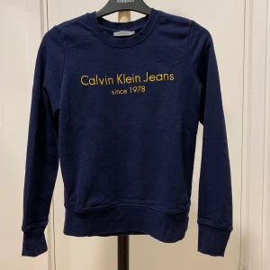 Calvin Klein tröja - Blå calvin klein tröja med gul tryck på bröstet. I väldigt bra skick. Storlek XS, passar också S.